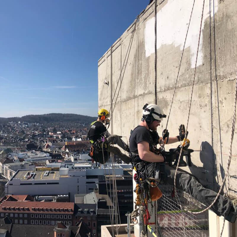 Höhenarbeiten mittels Seilzugangstechnik - Mitarbeiter beim Bohren in der Höhe